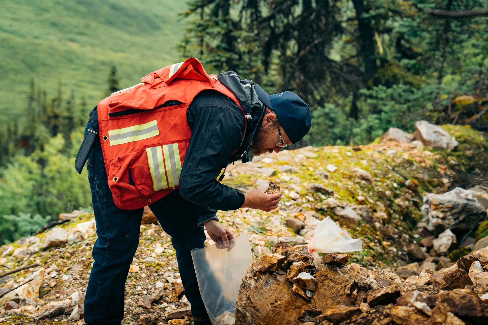 A geologist in a high-visibility vest examining a rock sample at Justin